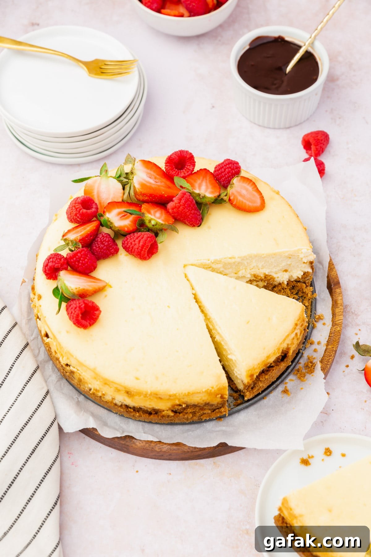 A gluten-free cheesecake topped with red berries with a slice already cut out of it.