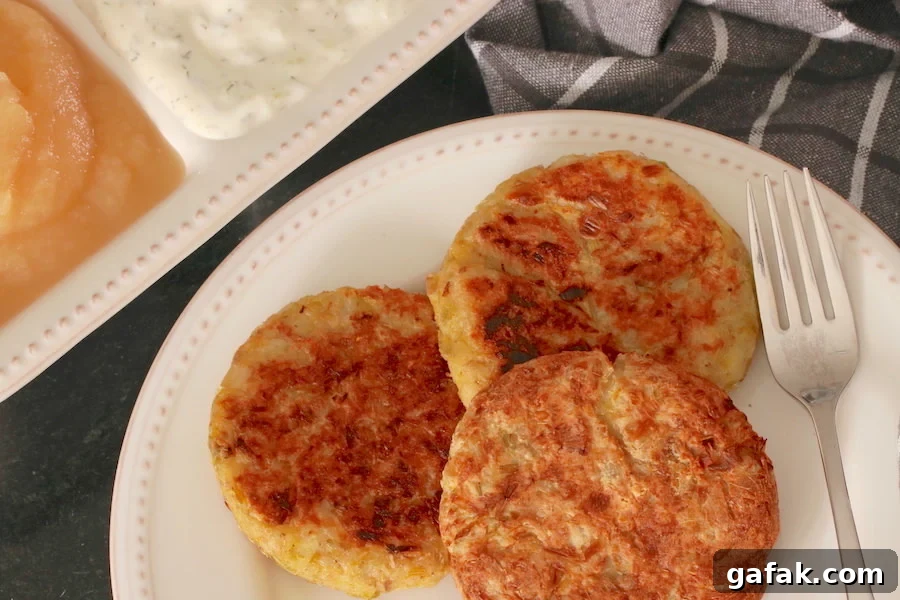 Three Vegan Potato Pancakes with Leeks plated; apple sauce and tzatziki sauce in the background and a checkered napkin to the side