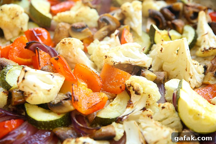 White balsamic roasted chopped zucchini, red onion, red bell pepper, mushrooms, and cauliflower on a baking sheet.