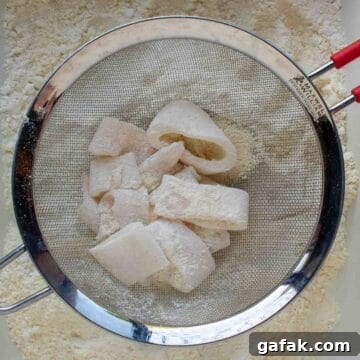 Flour coated calamari in a sieve to remove excess flour.