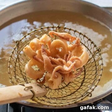 Fried calamari in a slotted spoon above an oil filled pan.