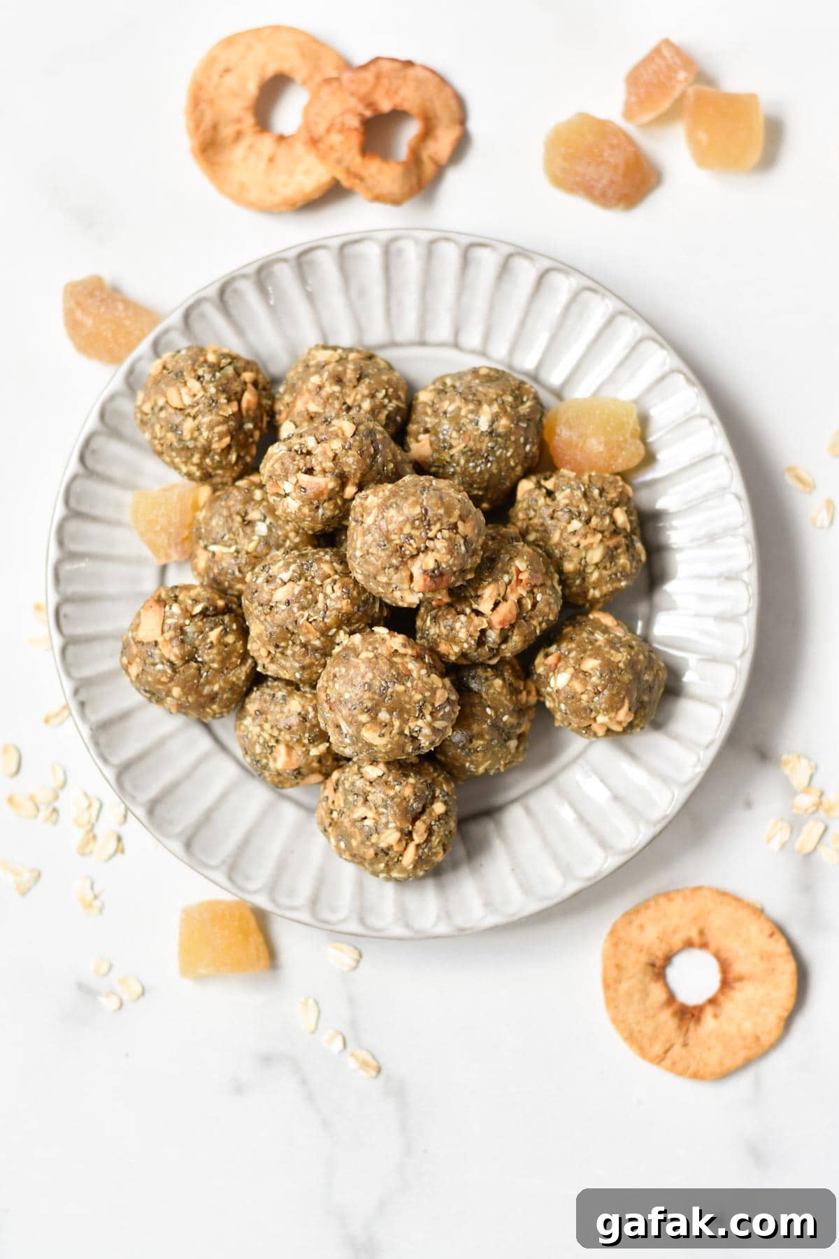 A stack of oatmeal protein balls on a gray plate with dried apple rings and ginger on the sides.