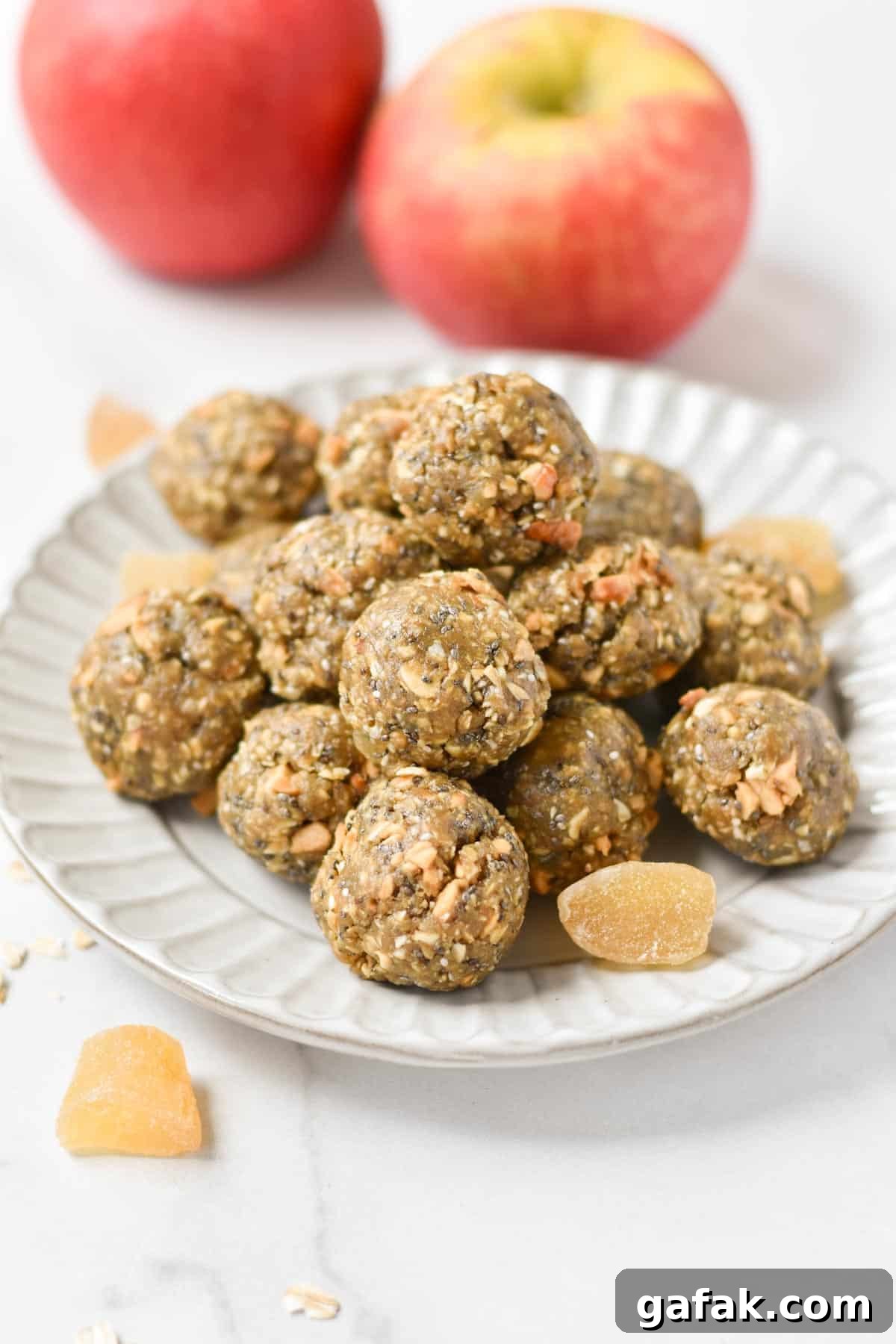 Energy balls with oats on a plate next to dried ginger and fresh apples.