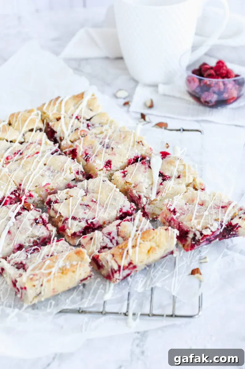 Sliced white chocolate raspberry blondies all cut up and placed on a metal cooling rack. White chocolate sauce has been drizzled over top.