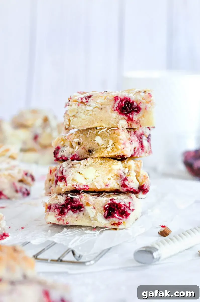 A stack of 4 blondie squares full of raspberries and white chocolate chips.