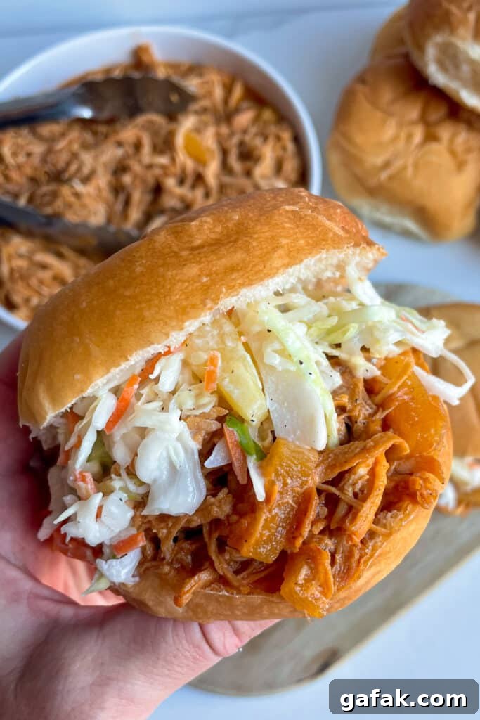 slow cooker Hawaiian chicken with pineapple slaw on a hamburger bun with pork in a serving bowl