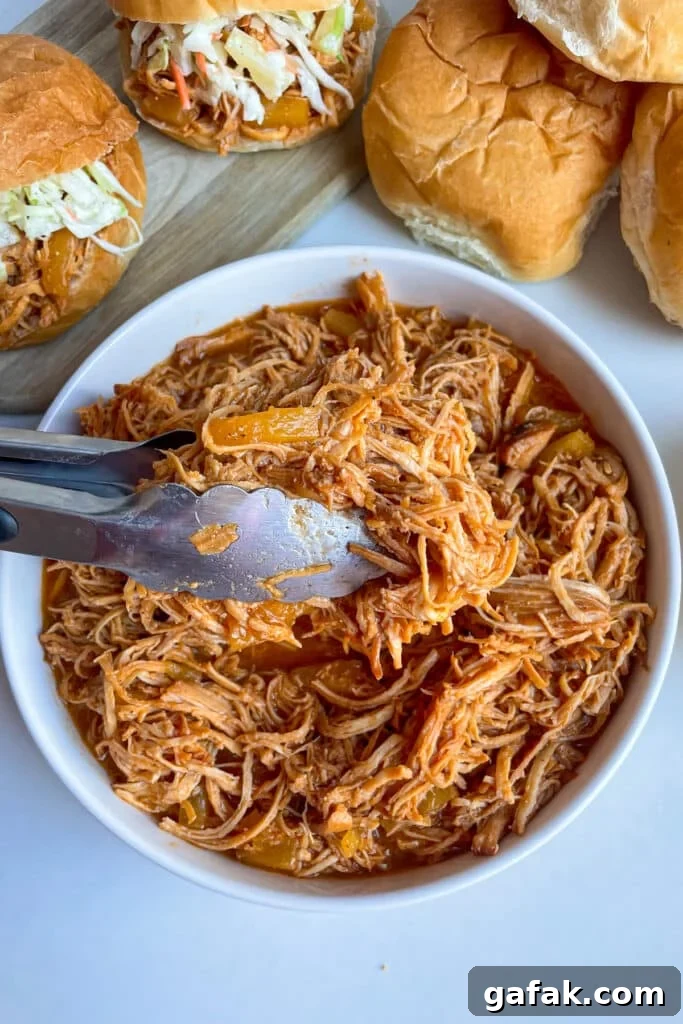 slow cooker Hawaiian chicken with pineapple slaw in a white serving bowl with buns for serving