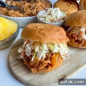 close up photo of slow cooker Hawaiian chicken with pineapple slaw on a hamburger bun with pineapple on the side