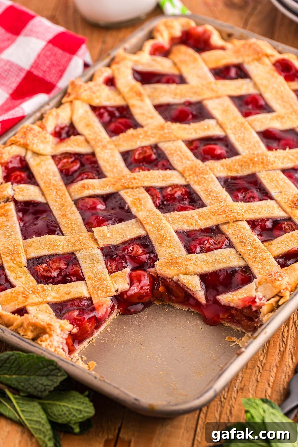 Cherry slab pie with a golden lattice crust in a rectangular pan, featuring neatly sliced pieces on a rustic wooden surface.