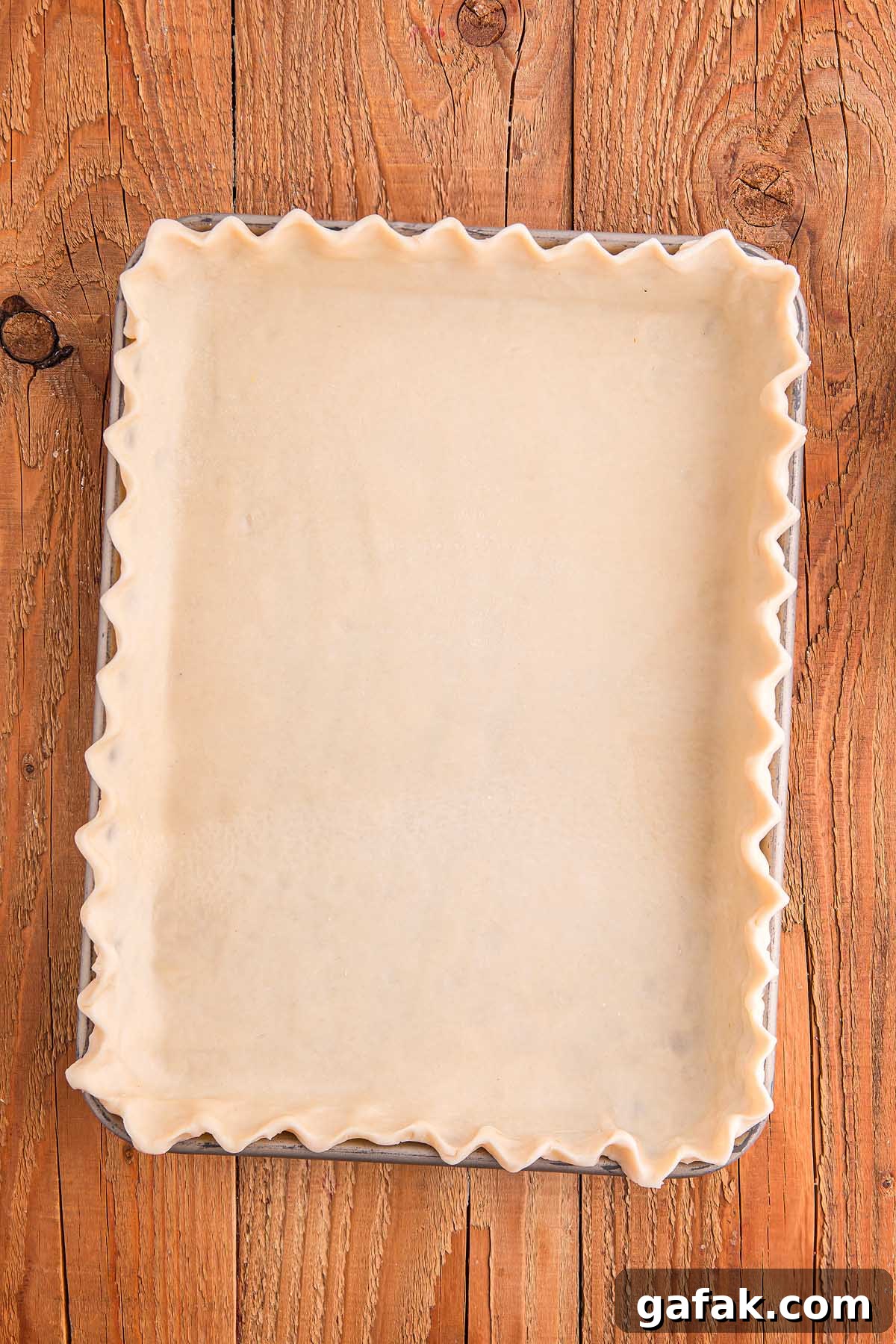 A rectangular cherry slab pie crust with crimped edges sits elegantly in a baking dish on a wooden surface.