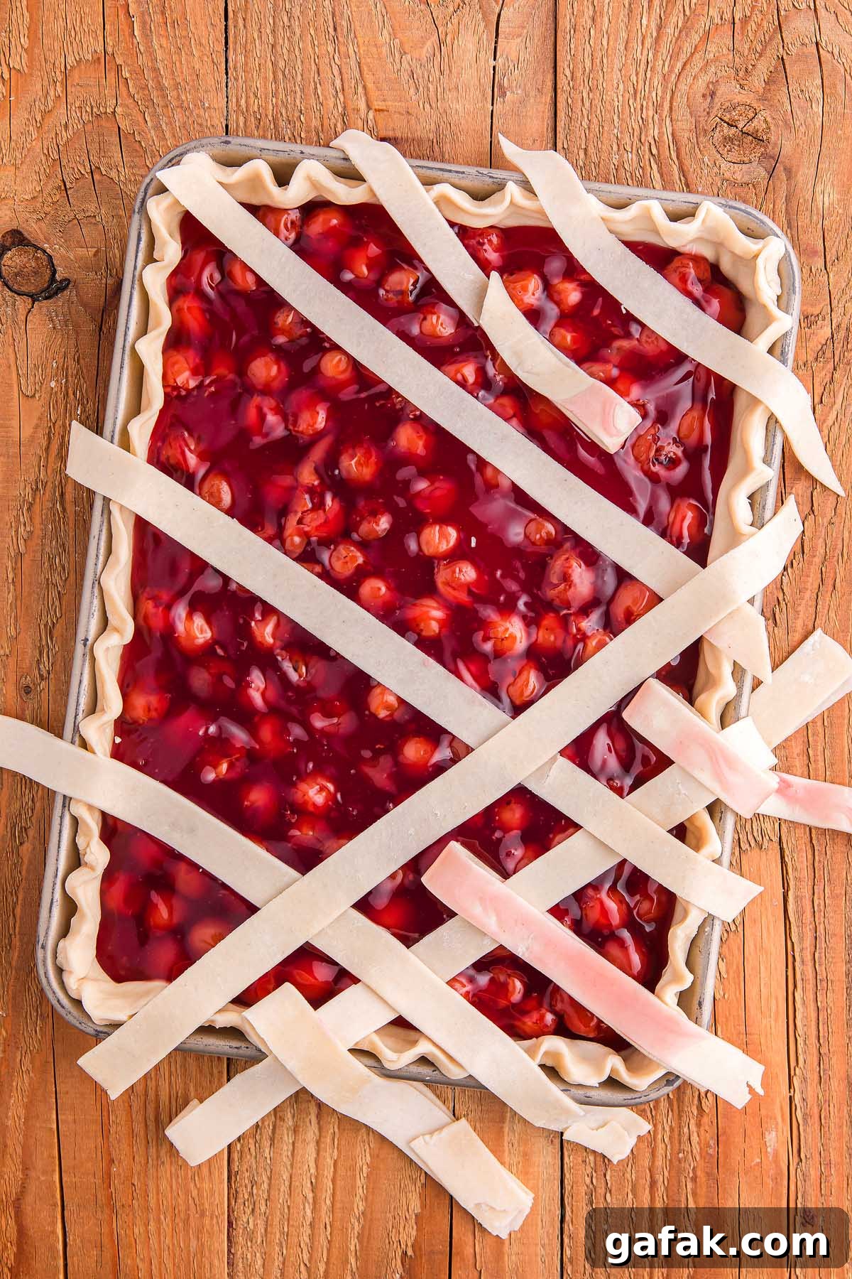 A cherry slab pie with an unfinished lattice crust rests on a wooden surface, offering a rustic charm.