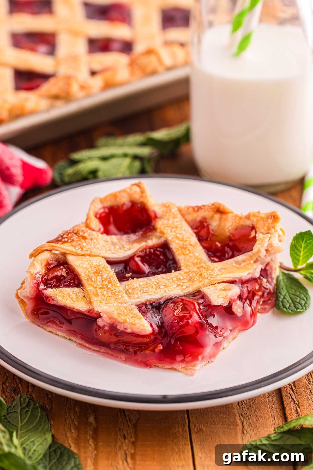 A slice of cherry lattice pie graces the plate, accompanied by a refreshing glass of milk and mint leaves, reminiscent of a classic cherry slab pie experience.