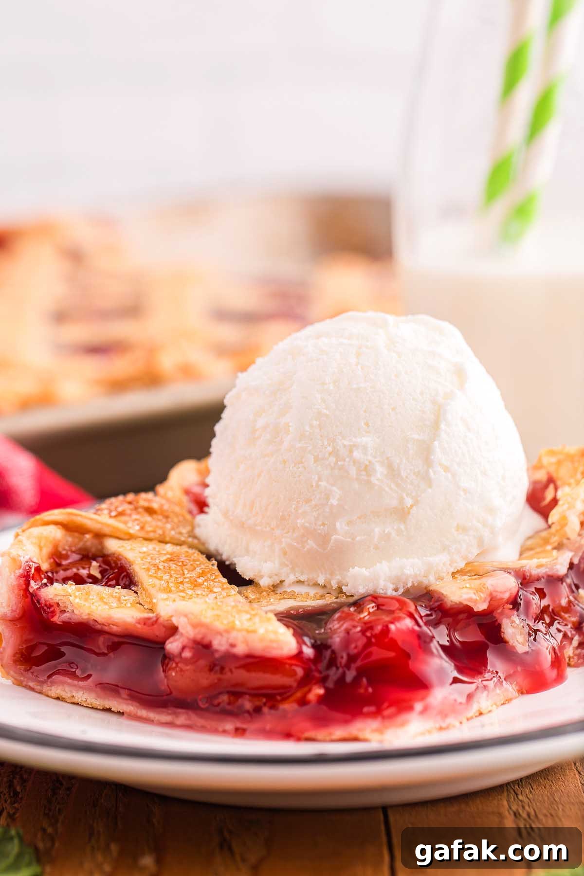 A slice of cherry slab pie with a scoop of vanilla ice cream rests elegantly on a white plate.