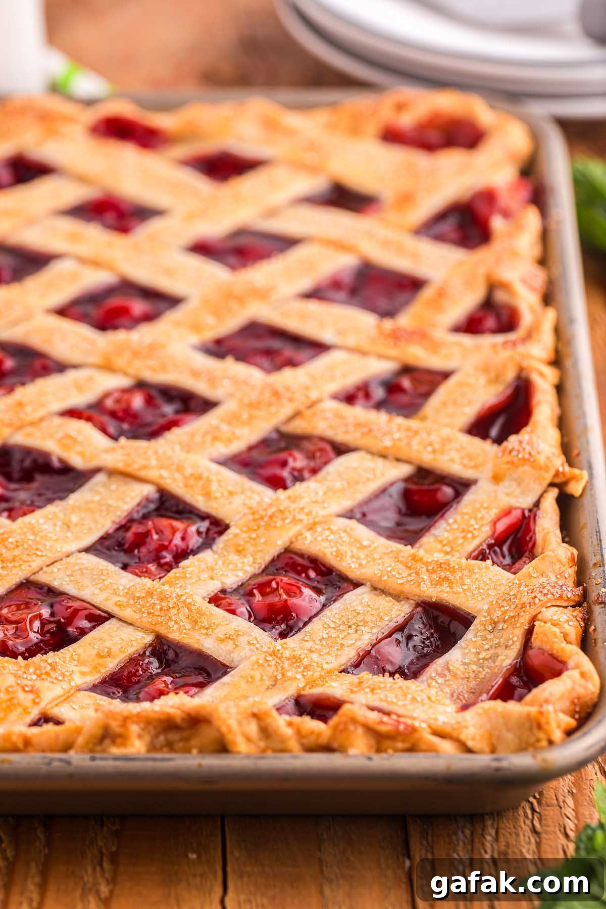 Cherry slab pie with a golden lattice crust rests invitingly in a rectangular pan on a wooden table.