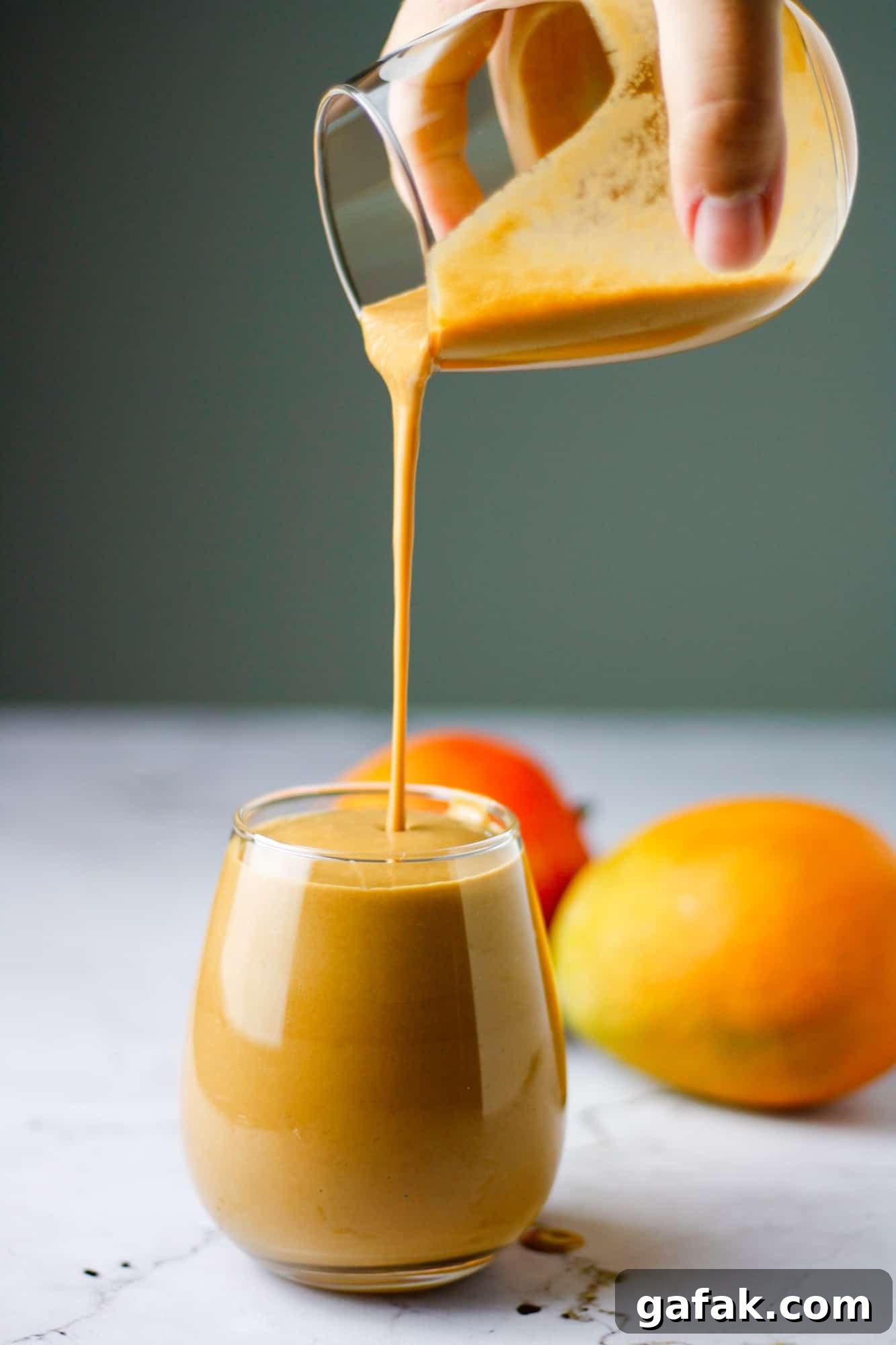 Chocolate Mango Smoothie Recipe for Creamy Tropical Shakes 2 Hand holding a glass of chocolate mango smoothie pouring it into another glass with mangos in the background