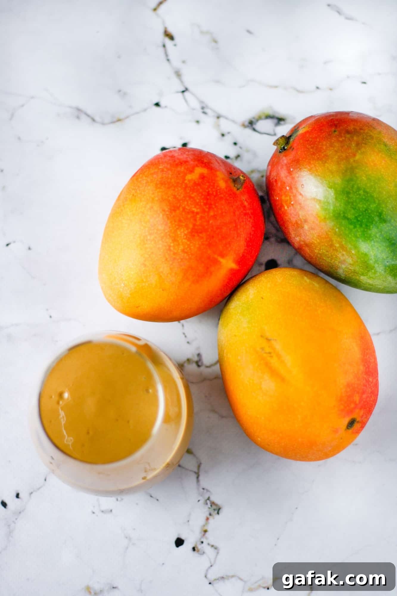 Chocolate Mango Smoothie Recipe for Creamy Tropical Shakes 4 Overheard angle of a glass of chocolate mango smoothie and three ripe mangos