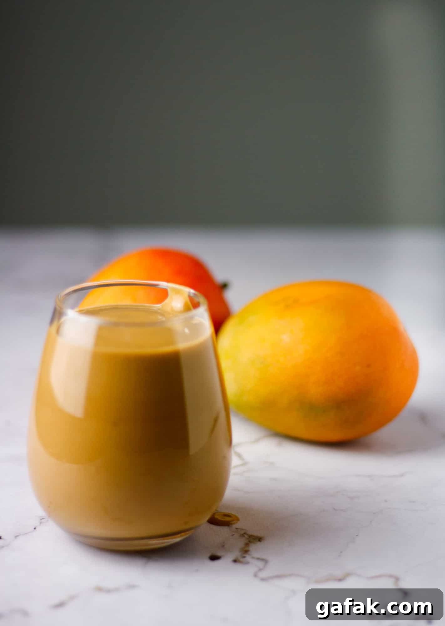 Chocolate Mango Smoothie Recipe for Creamy Tropical Shakes 7 A glass of chocolate mango smoothie on the table with mangoes in the background