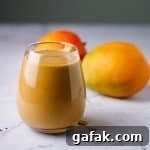 Glass of chocolate mango smoothie on table with mangoes in background