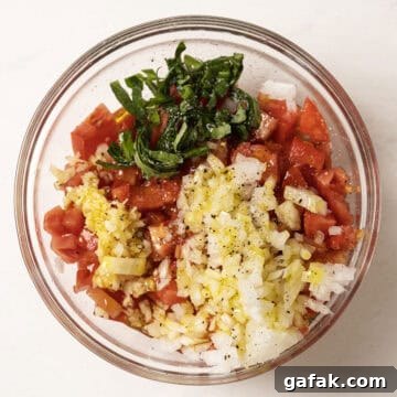 Tomatoes with onion, garlic, basil, olive oil, salt and pepper, in a bowl.