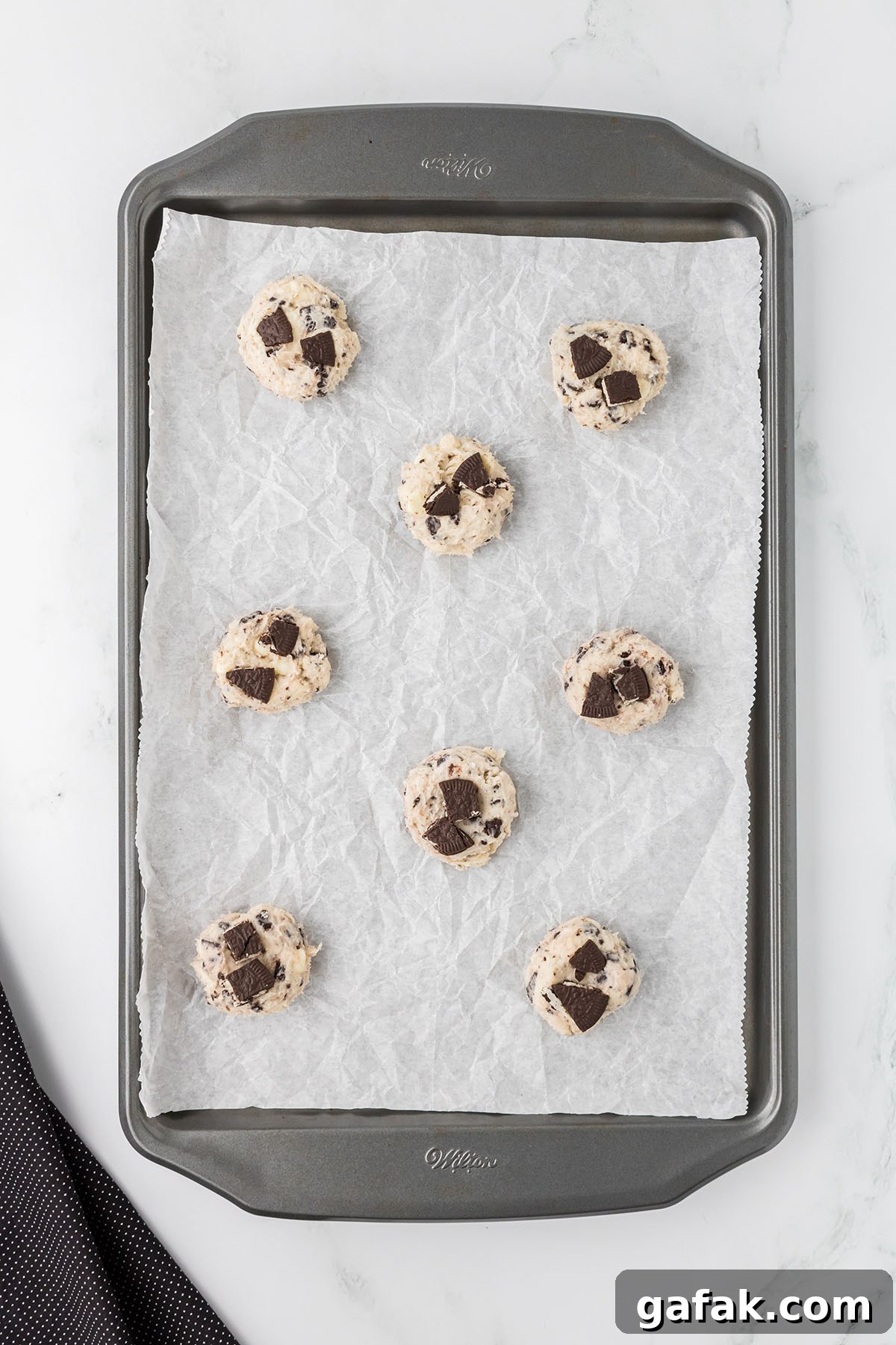 Crushed Oreos are placed on top of the cookie dough balls on the baking sheet.