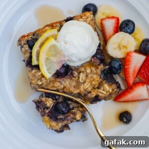 A square of blueberry oatmeal bake on a plate topped with whipped cream and fresh fruit.