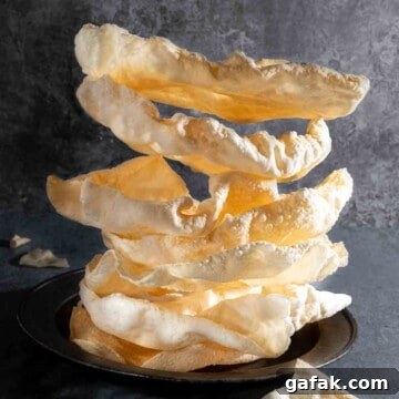 A pile of poppadoms on a plate against a grey background.