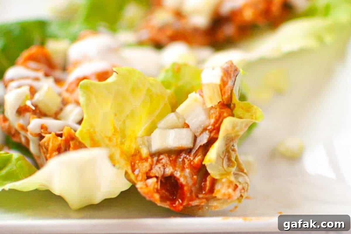 21 Packed Lunch Ideas to Make Midday Meals Exciting Again 13 Close-up of a lettuce leaf topped with shredded meat in sauce, diced onions, and a drizzle of white dressing, on a white plate.