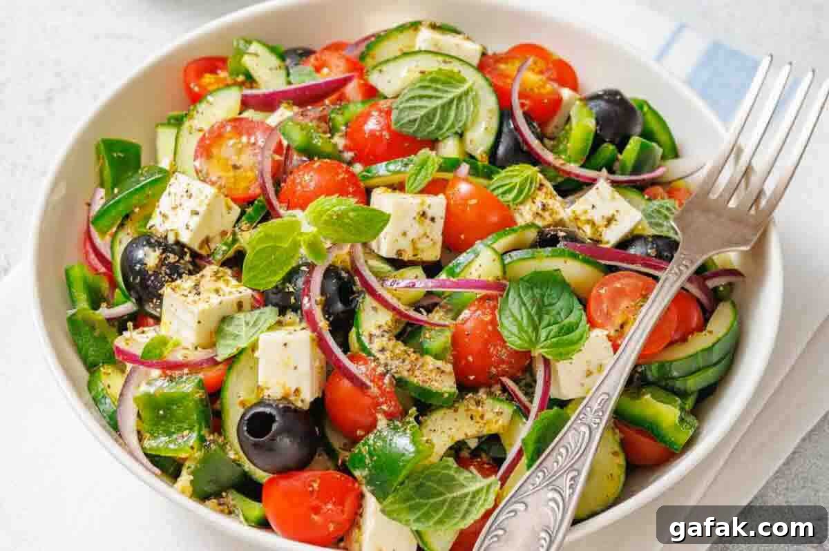 21 Packed Lunch Ideas to Make Midday Meals Exciting Again 22 A bowl of salad with feta cheese, cherry tomatoes, cucumber, red onion, black olives, green peppers, and fresh mint, served with a fork.