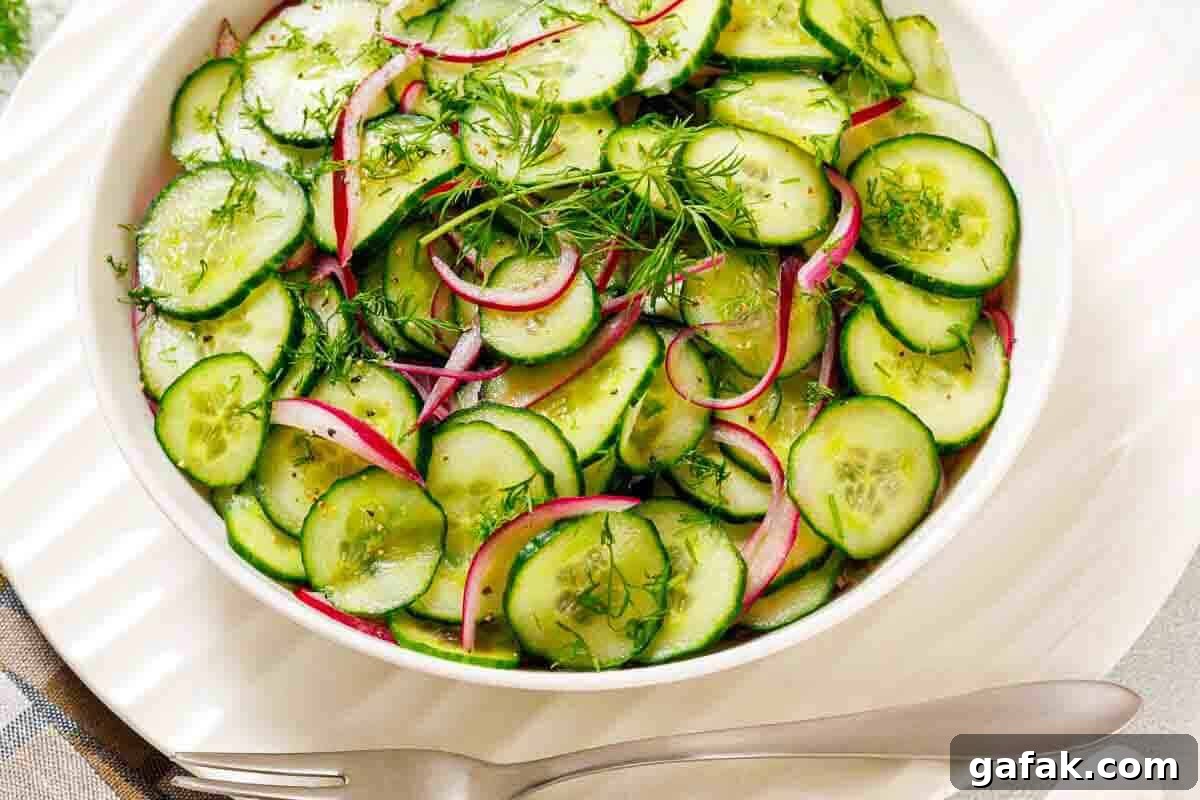 21 Packed Lunch Ideas to Make Midday Meals Exciting Again 5 A white bowl filled with sliced cucumbers, red onions, and fresh dill, placed on a white plate with a fork and spoon beside it.
