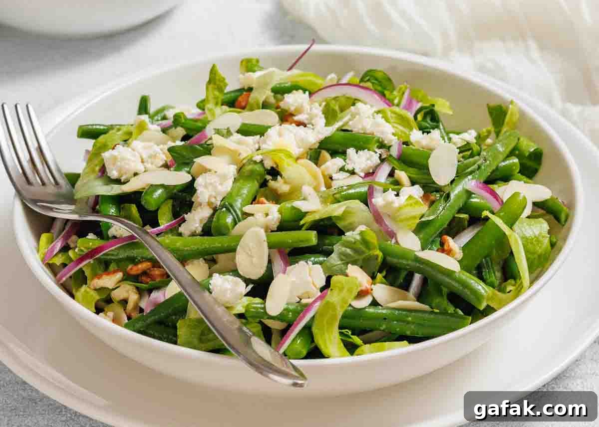 21 Packed Lunch Ideas to Make Midday Meals Exciting Again 7 A bowl of green bean salad with feta cheese, sliced almonds, red onions, and lettuce, served with a fork and spoon.