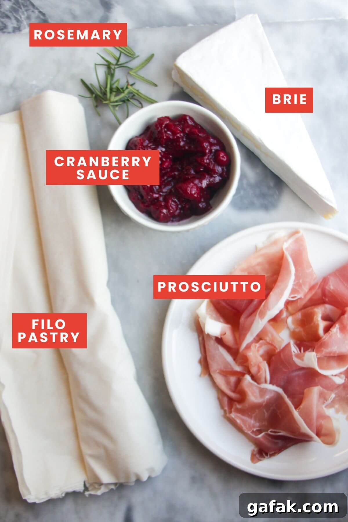 Ingredients for brie, cranberry and prosciutto filo bites laid out on a grey marble background and labelled.