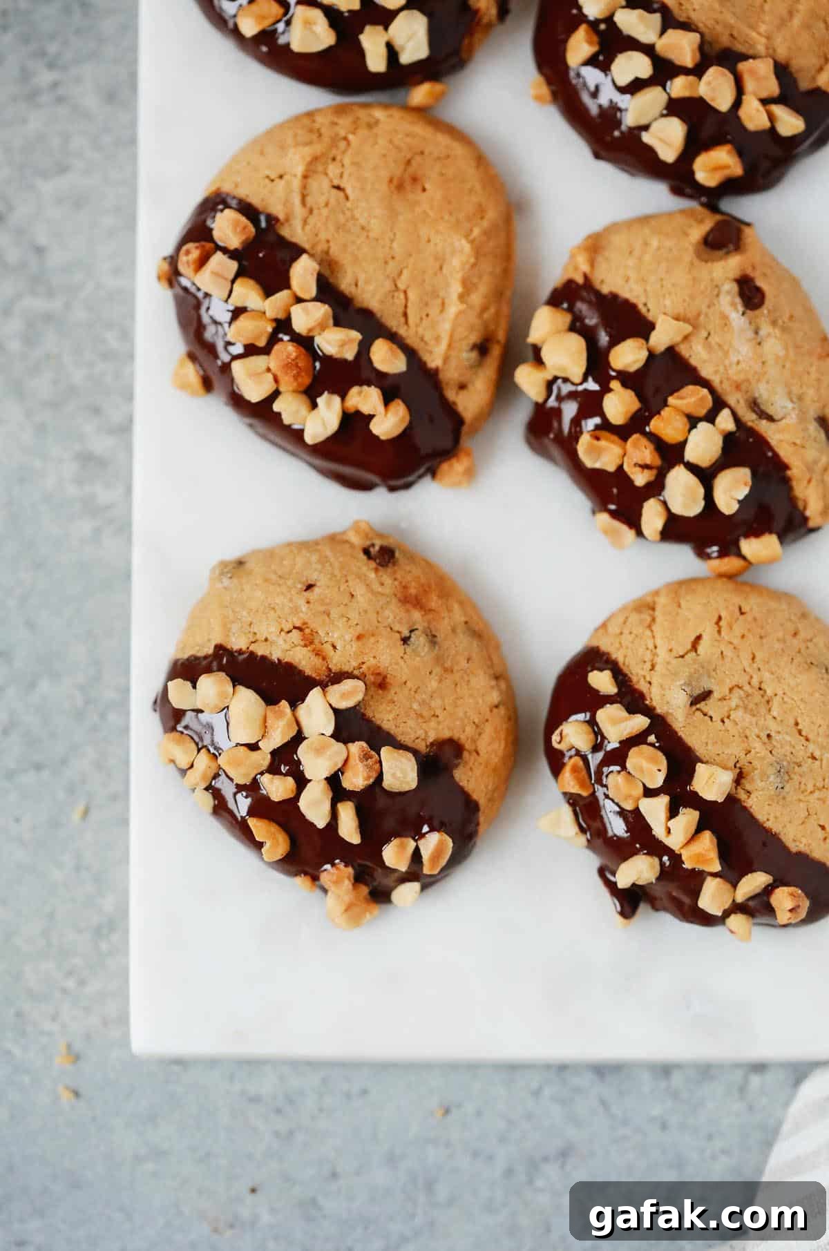 Overhead photo of multiple low-carb peanut butter cookies dipped in chocolate and topped with chopped peanuts on a white serving platter. 