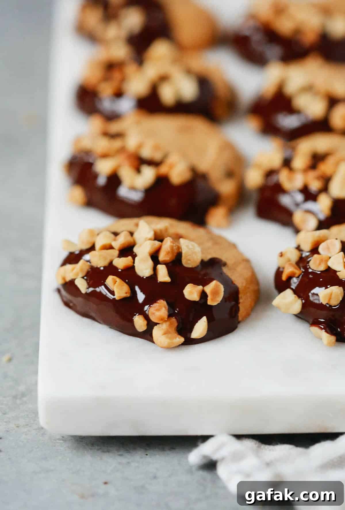 Multiple low-carb peanut butter cookies dipped in chocolate and topped with chopped peanuts. 