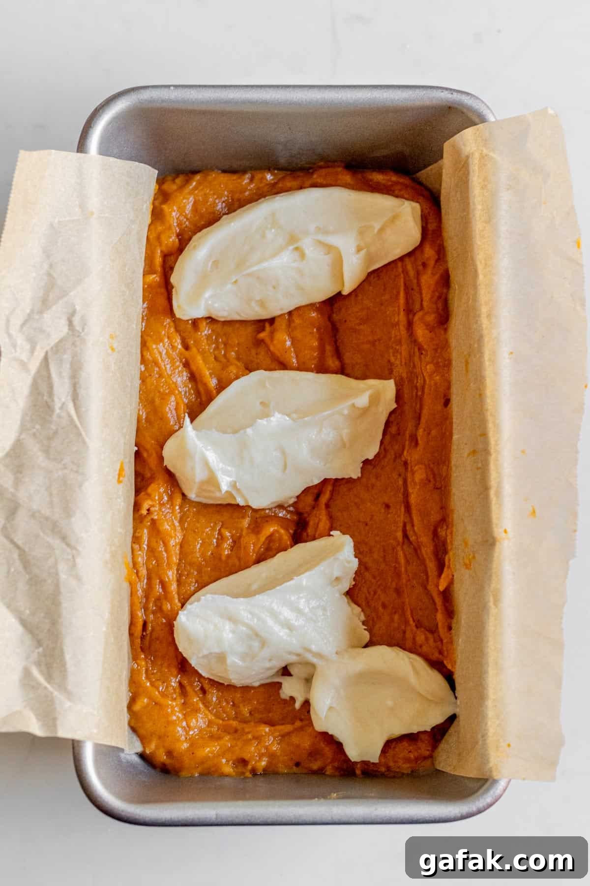 dollops of cream cheese on top of pumpkin bread batter in a loaf pan