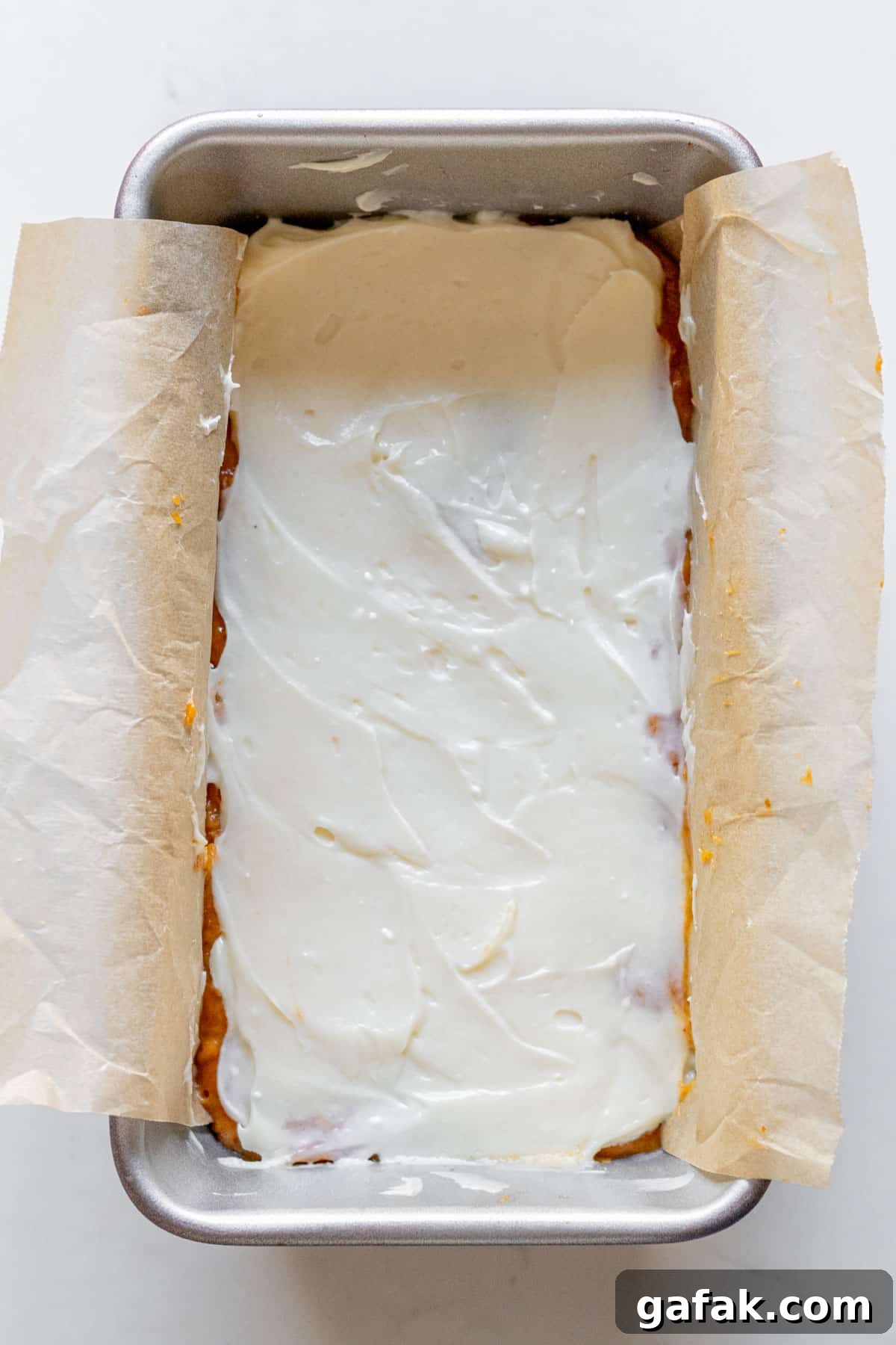 cream cheese spread over pumpkin bread batter in a loaft pan