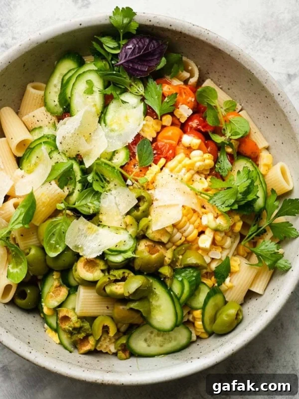 Bowl of pasta salad with cucumbers, tomatoes, olives, corn, and fresh herbs.