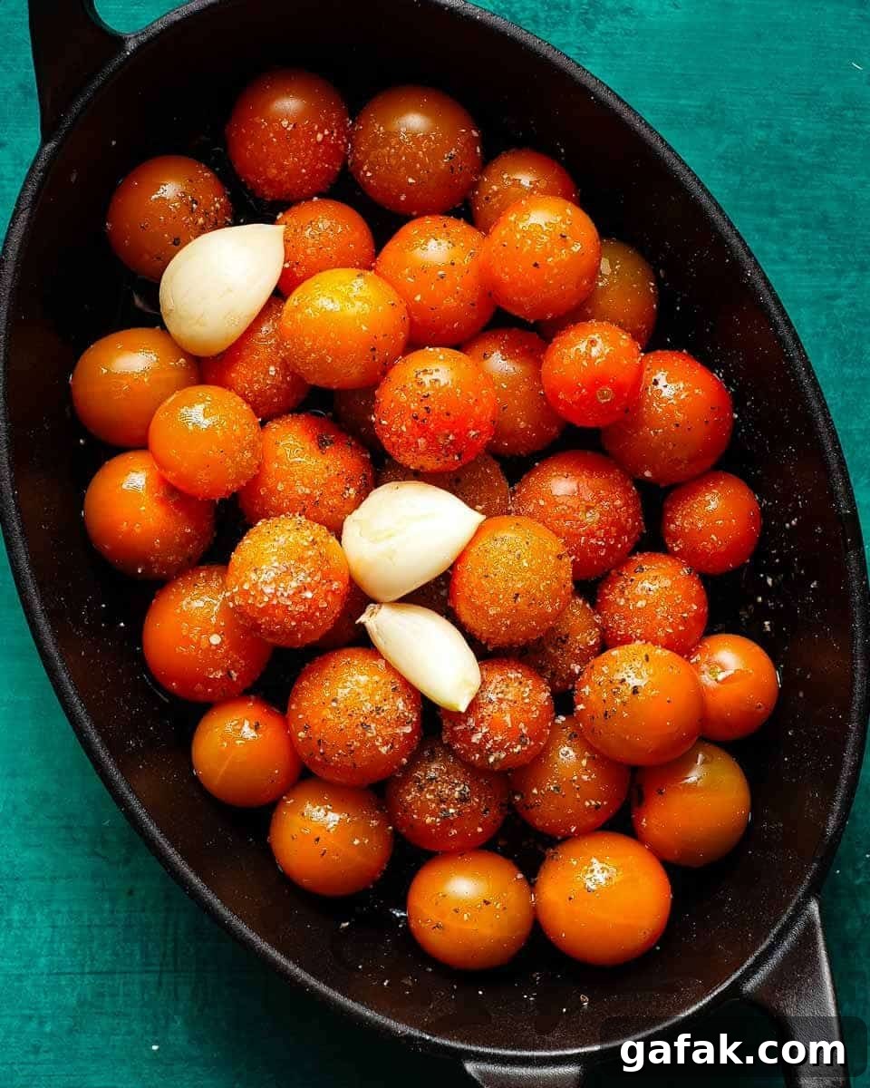 Seasoned Sungold tomatoes and garlic cloves in a black roasting pan.