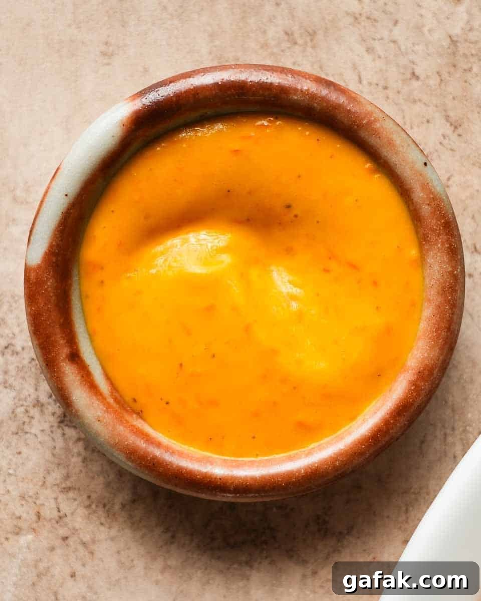 A small bowl of creamy orange sauce on a textured surface.