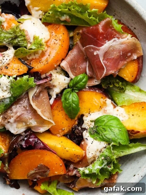 Salad with peaches, burrata, prosciutto, fresh greens, and basil leaves on a plate.