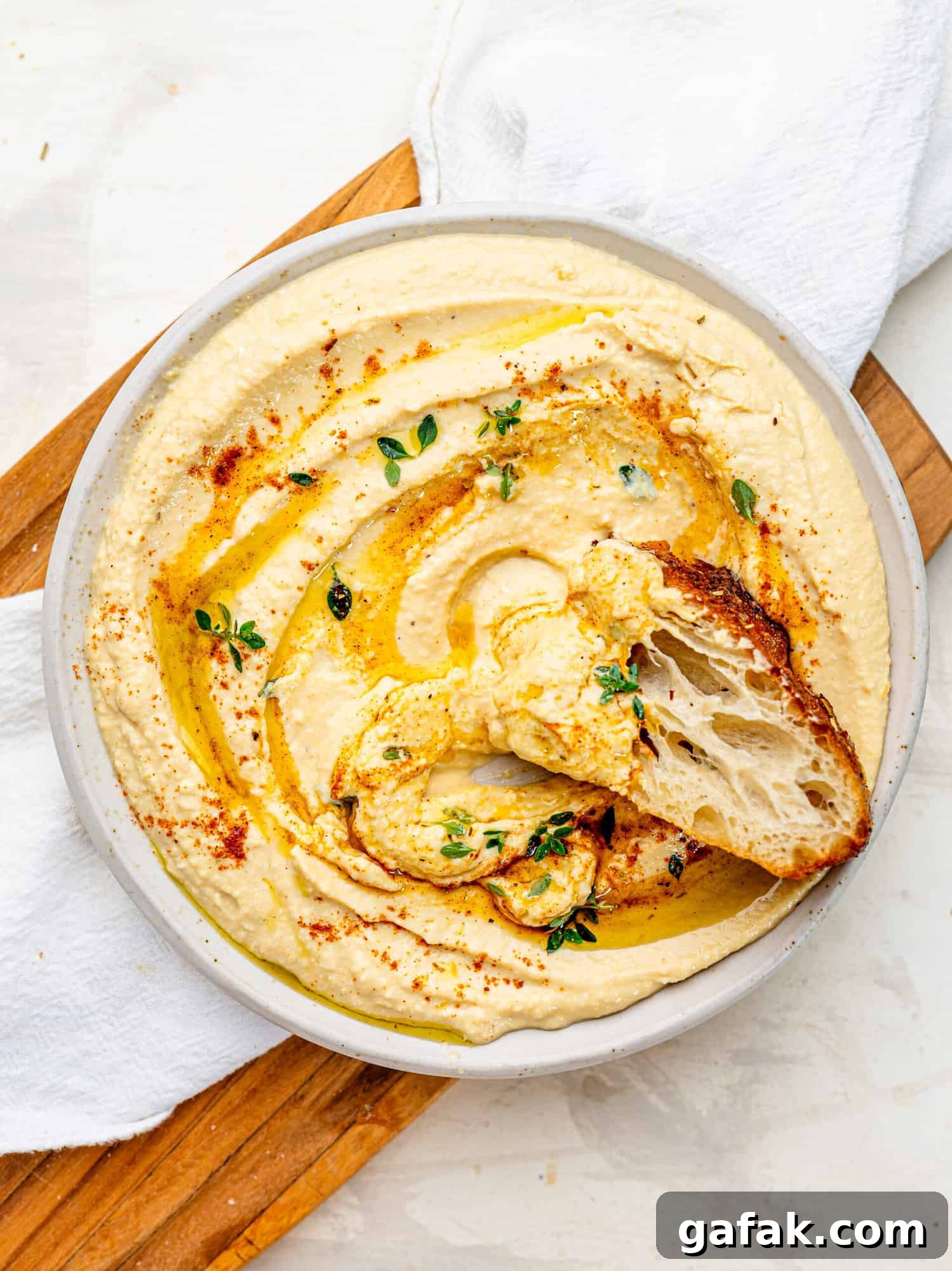 Creamy Cottage Cheese Hummus with a drizzle of olive oil spread out on a plate. There is a piece of foccaccia dipped into the hummus.