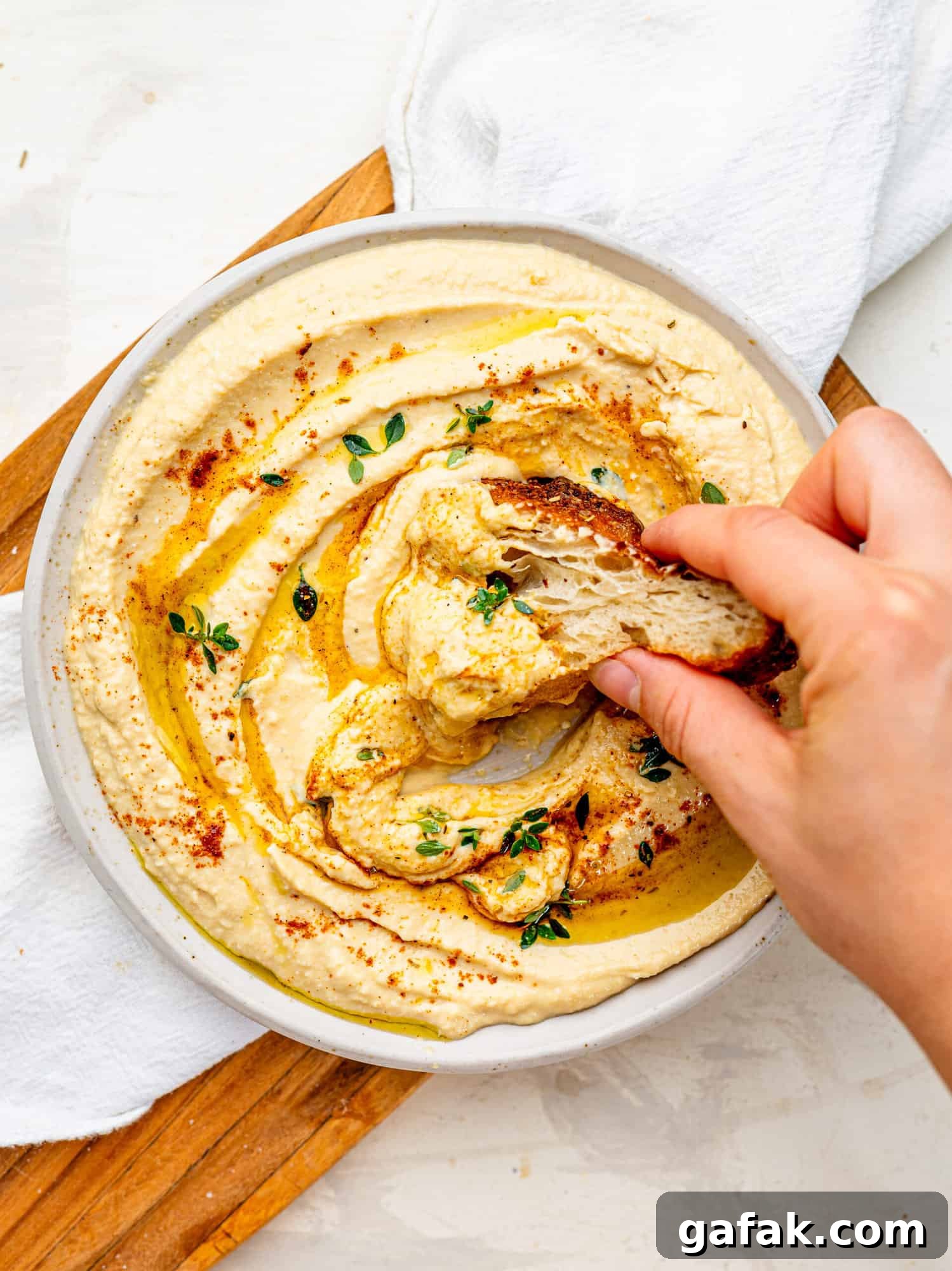 Creamy Cottage Cheese Hummus with a drizzle of olive oil spread out on a plate. Someone is dipping a piece of focaccia in it.