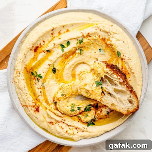 Creamy Cottage Cheese Hummus with a drizzle of olive oil spread out on a plate. There is a piece of foccaccia dipped into the hummus.