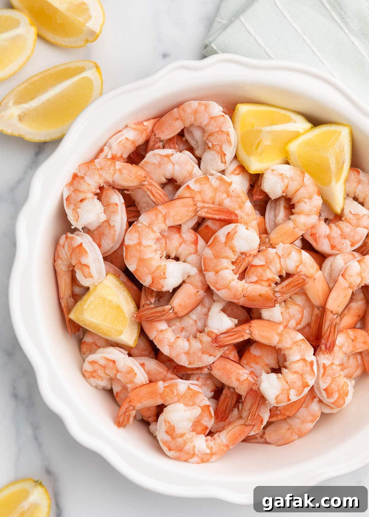 How to Poach Shrimp Perfectly Every Time 2 overhead of poached shrimp in a white fluted pie plate on a marble board with lemon wedges