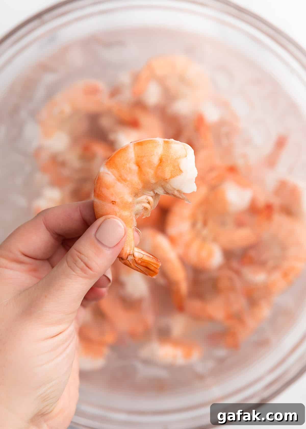 How to Poach Shrimp Perfectly Every Time 12 closeup of an unpeeled poached shrimp being held over a bowl of cooked shrimp