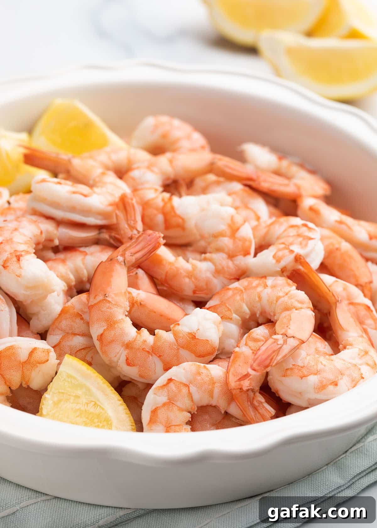 How to Poach Shrimp Perfectly Every Time 14 peeled poached shrimp in a white pie plate with lemon wedges