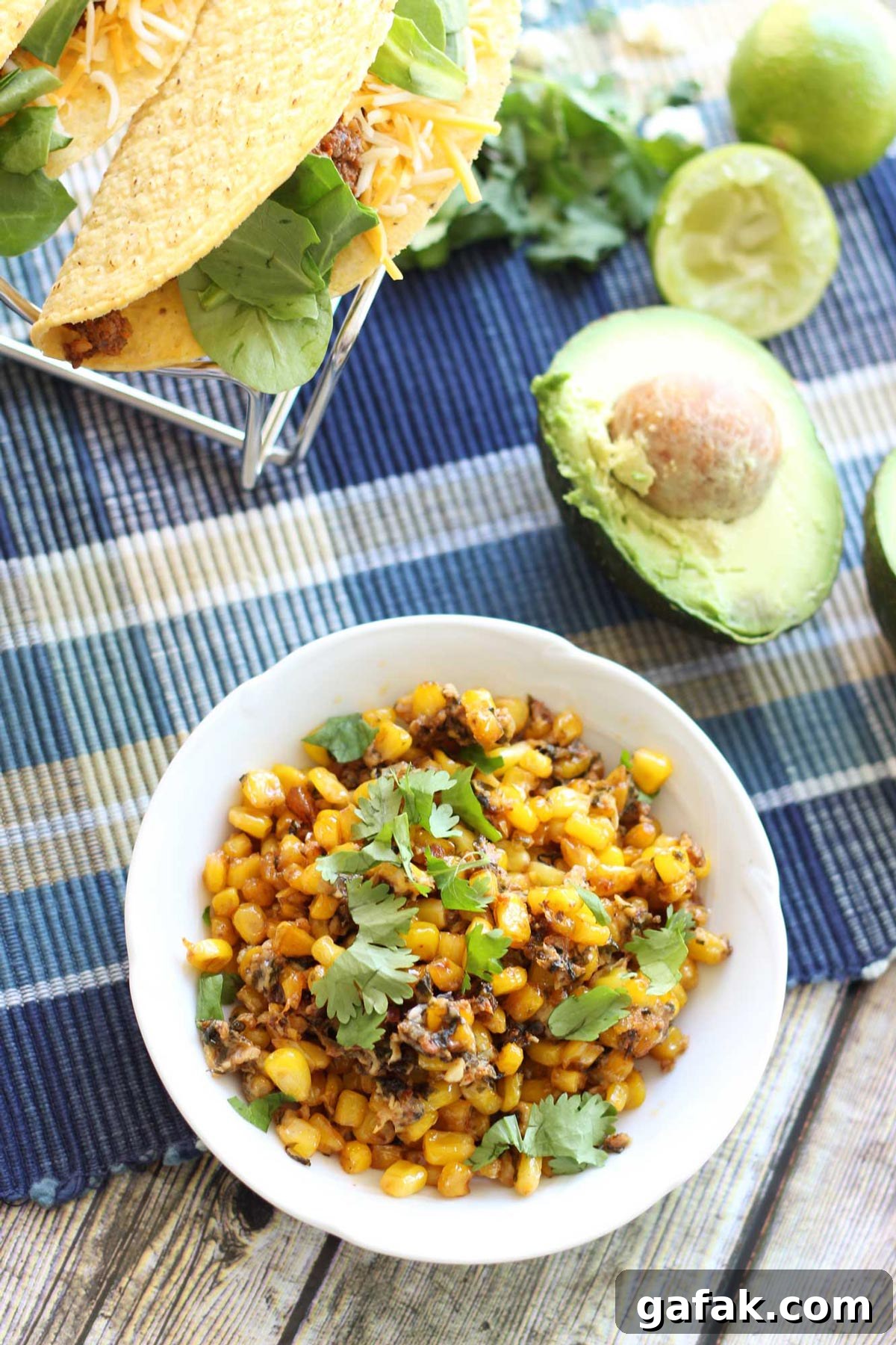 Authentic Mexican Street Corn (Elote) Recipe — Grilled & Creamy 3 Bowl of mexican street corn on a table beside beef tacos and avocado.
