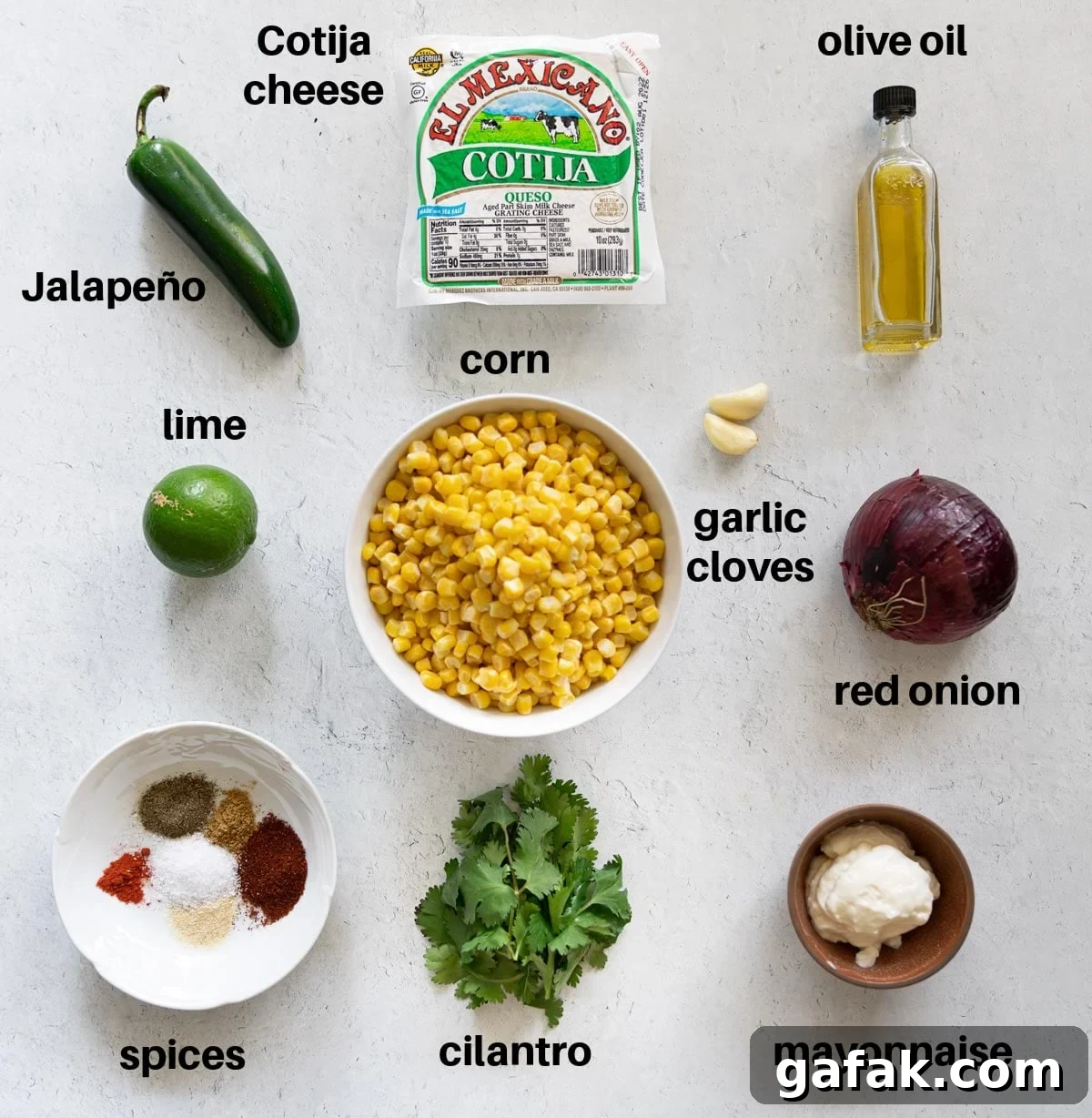 Authentic Mexican Street Corn (Elote) Recipe — Grilled & Creamy 4 Kernels of corn, Cotija cheese, olive oil, onion, mayonnaise, spices, cilantro, lime, and jalapeno on a counter.