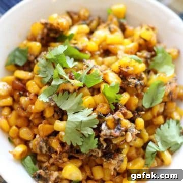 White bowl containing Mexican Street Corn topped with fresh cilantro sitting on a blue tablecloth.