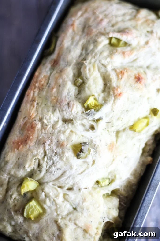 a loaf of dill pickle bread shown in a dark metal loaf pan