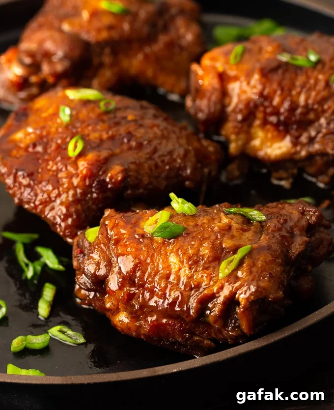 A plate of shoyu chicken with thickened brown sauce and green onion garnish.